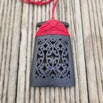 Ebony wood 3d printed toki pendant with red binding on wooden surface, front view