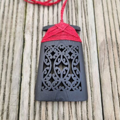 Ebony wood 3d printed toki pendant with red binding on wooden surface, front view