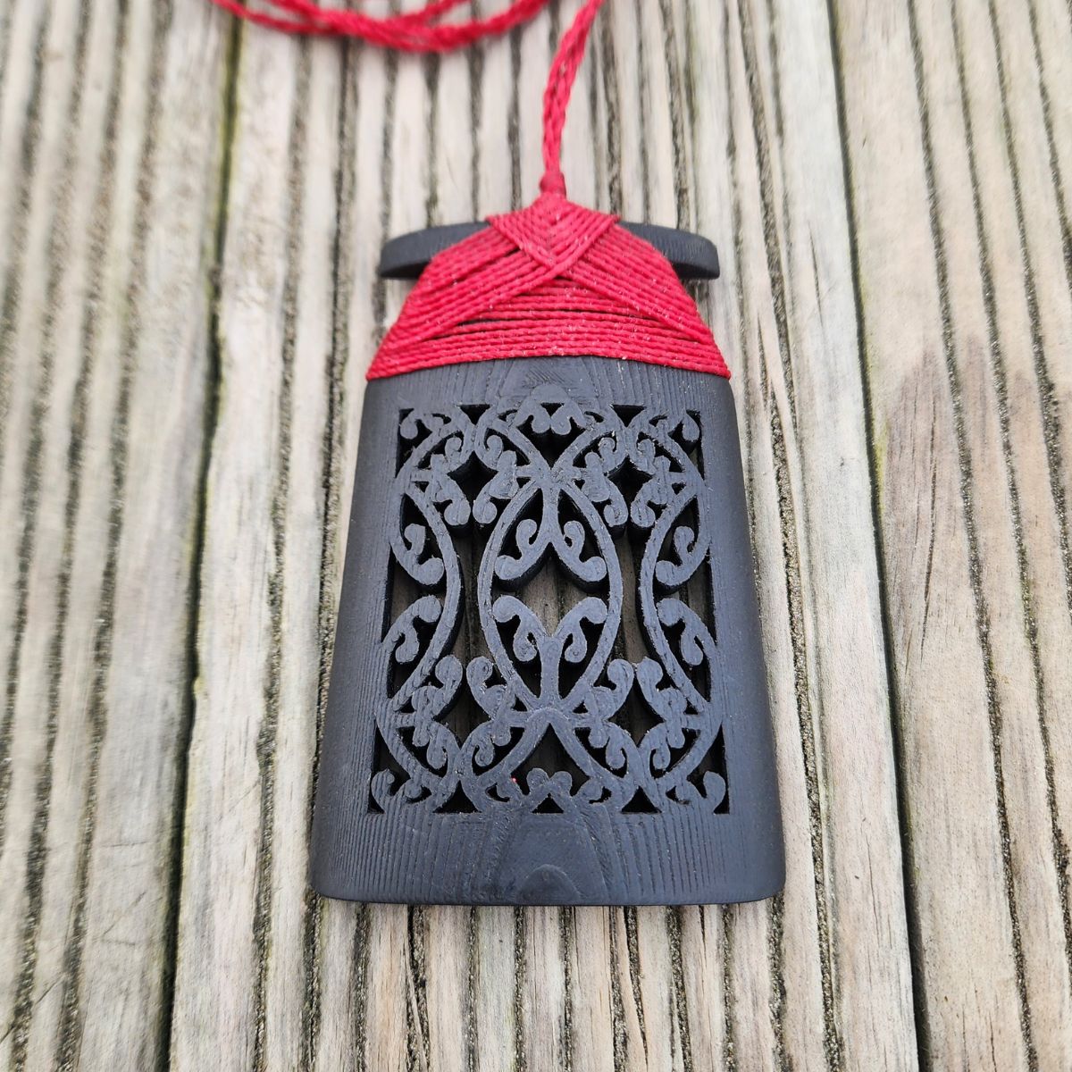 Ebony wood 3d printed toki pendant with red binding on wooden surface, front view