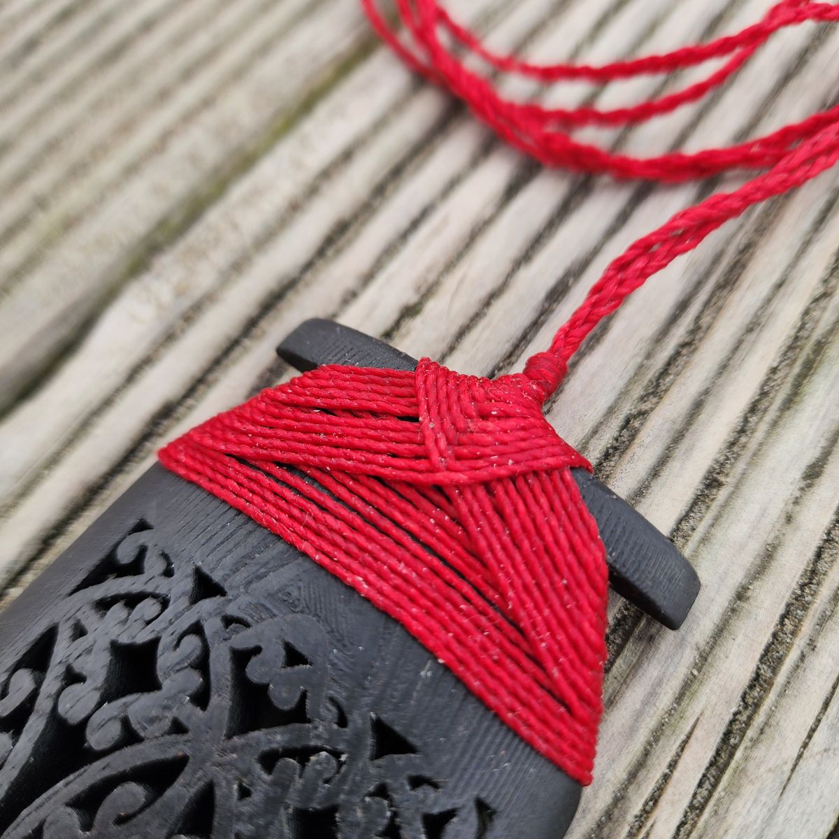 close up of red binding on ebony wood toki pendant