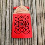 red coloured 3d printed toki necklace with natural coloured binding and cord, on a wooden surface, front view