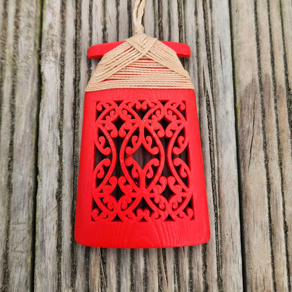 red coloured 3d printed toki necklace with natural coloured binding and cord, on a wooden surface, front view