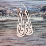 bone white mangōpare toki earrings propped up against driftwood at the beach