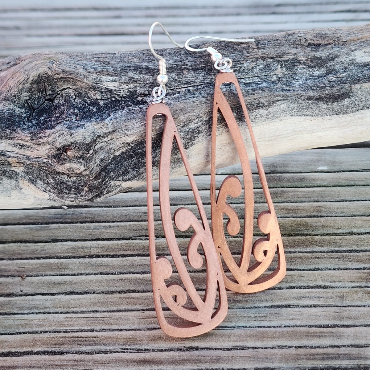 The copper mangōpare earrings against a piece of beach driftwood