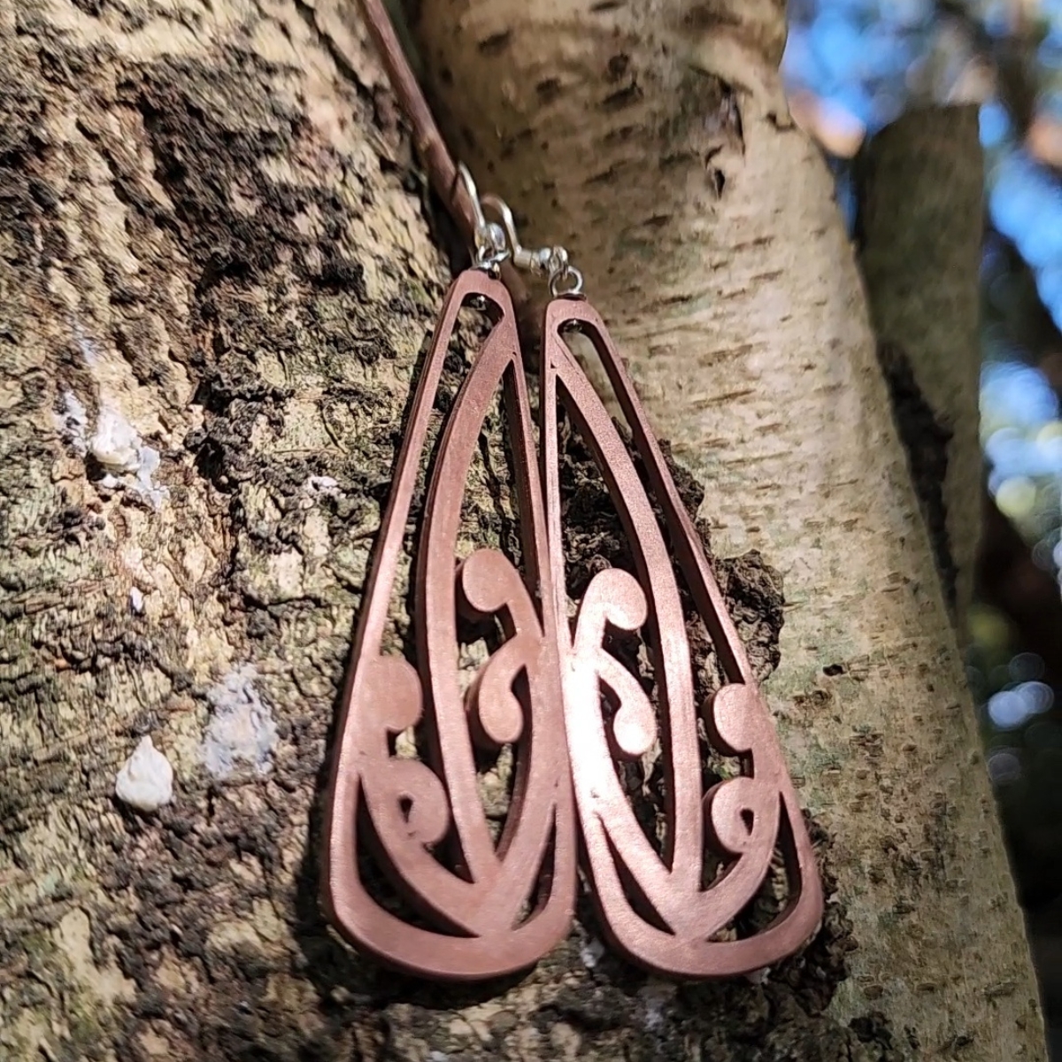 closeup view of the copper mangōpare toki earrings against native wood bark
