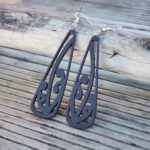 Ebony wood black mangōpare toki earrings against driftwood at the beach