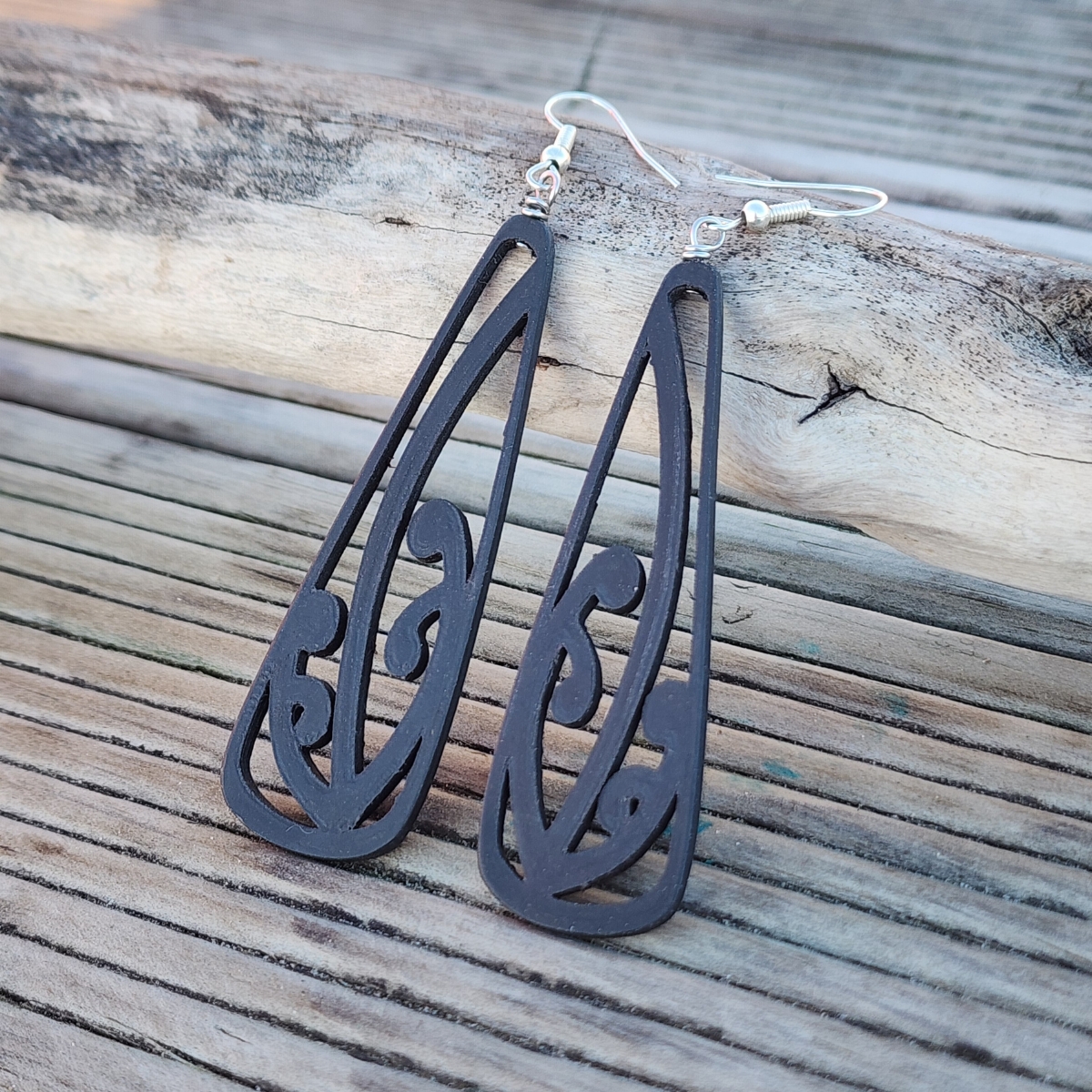 Ebony wood black mangōpare toki earrings against driftwood at the beach